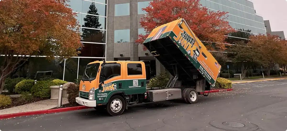 Take Care Junk Hauling dump truck with its bed raised outside a Sacramento office building